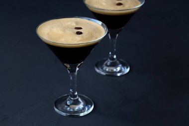 Masada kahve çekirdekleri ile süslenmiş espresso martini kokteylleri. Siyah arka planda iki martini bardağı. alkollü içecek
