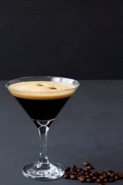 Masada kahve çekirdekleri ile süslenmiş espresso martini kokteylleri. Siyah arka planda martini bardağı. Dikey. alkollü içecek