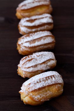 Masada Fransız eklerleri var. Tahta bir masada vanilya eklerleri ya da profiteroller. Esmer arka planda geleneksel Fransız tatlısı. kopyalama alanı. dikey