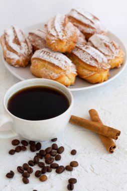 Ev yapımı vanilya eklerleri ya da beyaz bir masadaki profiteroller. kopyalama alanı. Geleneksel Fransız usulü tatlı ve kahve fincanı, kahve çekirdekleri ve tarçın çubukları beyaz masada. dikey