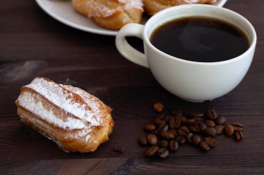 Ev yapımı vanilyalı ekler ya da ahşap bir masada beyaz bir tabakta profiterol. kopyalama alanı. Esmer arka planda geleneksel Fransız tatlısı. Fasulyeli sade kahve..