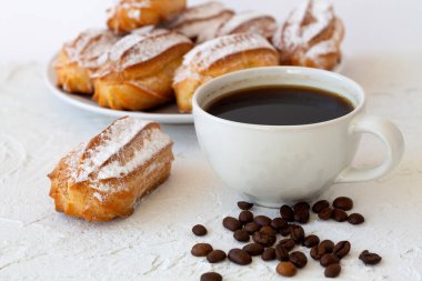 Beyaz bir masada vanilya eklerleri ya da profiteroller. kopyalama alanı. Geleneksel Fransız Lezzetli tatlı ve kahve fincanı beyaz masada kahve çekirdekleri.