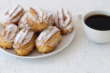 Ev yapımı vanilya eklerleri ya da beyaz bir masadaki profiteroller. kopyalama alanı. Geleneksel Fransız tatlısı ve arka planda bir fincan sade kahve..