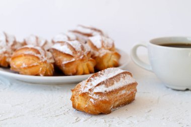 Ev yapımı vanilya eklerleri ya da beyaz bir masadaki profiteroller. kopyalama alanı. Geleneksel Fransız tatlısı ve arka planda bir fincan sade kahve..