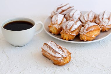 Ev yapımı vanilya eklerleri ya da beyaz bir masadaki profiteroller. kopyalama alanı. Geleneksel Fransız tatlısı ve arka planda bir fincan sade kahve..