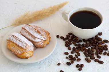 Masada eklerli bir tabak. Beyaz arka planda kahve çekirdekleri olan kahve fincanı. Geleneksel Fransız tatlısı. en üstteki görünüm
