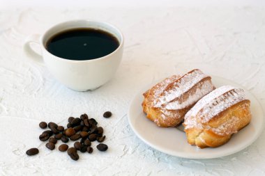 Masanın üstünde geleneksel Fransız ekmekleri. Beyaz arka planda kahve çekirdekleri olan kahve fincanı. Lezzetli tatlı.