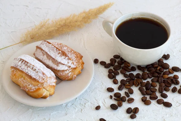 Masada eklerli bir tabak. Beyaz arka planda kahve çekirdekleri olan kahve fincanı. Geleneksel Fransız tatlısı. en üstteki görünüm