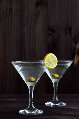 Barda iki bardak margarita kokteyli. Ahşap zemin üzerinde zeytin olan martini bardakları. Siyah masada limonlu ve yeşil naneli martini için bardaklar. kopyalama alanı. alkollü içecek.