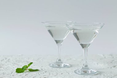 Beyaz arka planda yeşil naneli iki martini bardağı. Alkollü. Kokteyl için bardaklar masaya. Boşluğu kopyala