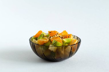 Beyaz arka planda cam kase içinde meyve salatası. Beyaz bir masada yeşil naneli meyveli bir kase sağlıklı salata. Karışık taze muz, portakal, kivi, meyve. Boşluğu kopyala.