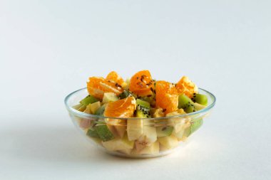 Beyaz arka planda cam kasede meyve salatası. Beyaz bir masada yeşil naneli meyveli bir kase sağlıklı salata. Karışık taze muz, portakal, kivi, meyve. kopyalama alanı. Sağlıklı vejetaryen yemeği.