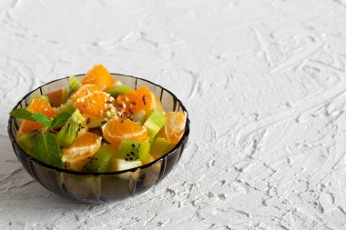 Beyaz bir masada yeşil naneli meyveli bir kase sağlıklı salata. Karışık taze muz, portakal, kivi, meyve. kopyalama alanı. Cam kasede meyve salatası, beyaz arka planda bir bardak süt..