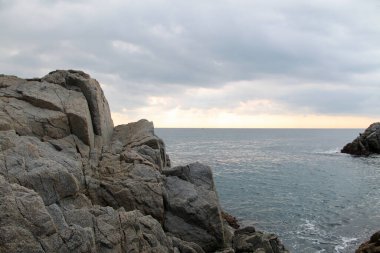 Denizde kayalar. Akdeniz manzarası çok güzel. Sahilde büyük taşlar, sakin su ve bulutlu gökyüzü arkaplanı. yaz gün batımı