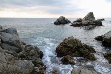 Sahildeki kayalar. Akdeniz manzarası çok güzel. Deniz dalgaları taşlarda kırılır. Kayaların yanında güneş ışığı olan mavi su