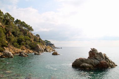 Denizde güzel bir ada. Akdeniz manzarası çok güzel. Deniz dalgaları taşlarda kırılır. Kayaların yanında güneş ışığı olan mavi su