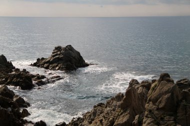Dalgalar kayalara çarpıyor. Sabah kumsalda. Akdeniz manzarası çok güzel. Denizde fırtına havası var. Etkileyici bir manzara. Denizin üzerindeki gri bulutlar. yaz gün batımı