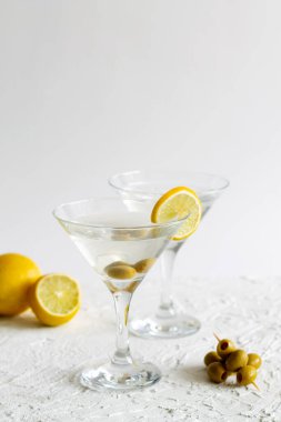 Kokteyl ve beyaz arka planda zeytinli iki martini bardağı. Limonlu ve limonlu kokteyl. kopyalama alanı. Alkollü. dikey.