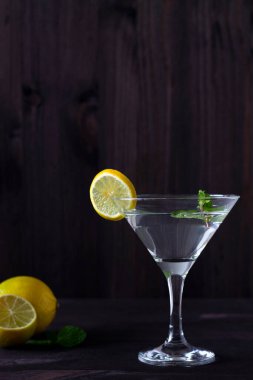 Siyah zemin üzerinde buz ve kokteyl olan martini bardağı. Limonlu kokteyl ve ahşap masada yeşil nane şekeri. kopyalama alanı. Alkollü. dikey