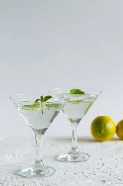 Alkollü. Beyaz arka planda kokteylli iki martini bardağı. Limonlu ve yeşil naneli Margarita kokteyli. kopyalama alanı. dikey