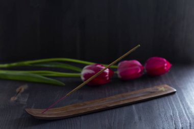 Siyah arka planda tütsü çubukları olan bir buket kırmızı lale. Tahta bir masada yeşil yapraklı üç pembe bahar çiçeği. Aromaterapi. Boşluğu kopyala.