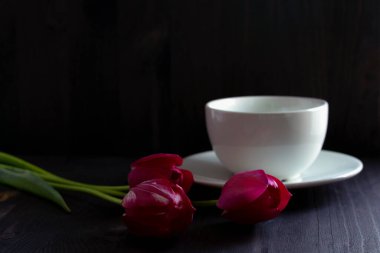 Kırmızı lalelerle dolu bir hayat. Beyaz kahve fincanı olan bir buket lale. Siyah arka planda parlak bahar laleleri. Uzayı kopyala Siyah masada kırmızı laleler. Seçici odak