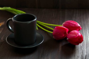 Sade kahve fincanı olan bir buket lale. Siyah arka planda parlak bahar laleleri. Uzayı kopyala Siyah masada kırmızı laleler. en üstteki görünüm.