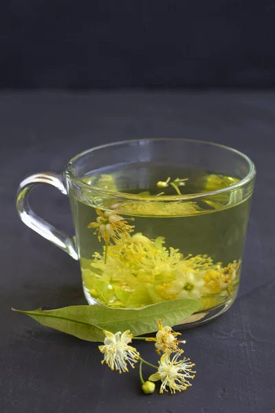 cup of tea.linden flowers tea.Cup of hot herbal tea with linden fresh flowers on a black table.Healthy lifestyle.glass cup of green tea with leaves on a black background.hot drinks.vertical