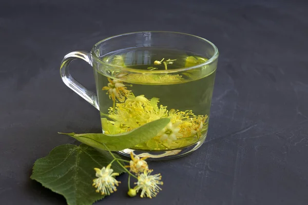 linden flowers tea.Cup of hot herbal tea with linden fresh flowers on a black table.Healthy lifestyle.glass cup of tea with green leaves on a black background.hot drinks.copy space