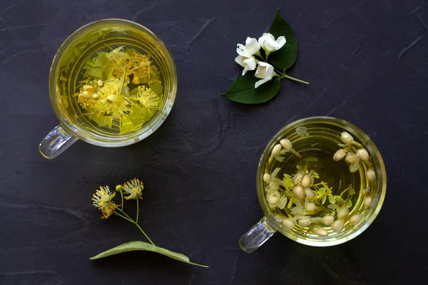 Jasmine tea and linden flowers tea.Cups of hot herbal tea with jasmine fresh flowers and linden on a black table.Healthy lifestyle.glass cup of green tea with leaves on a black background.top view