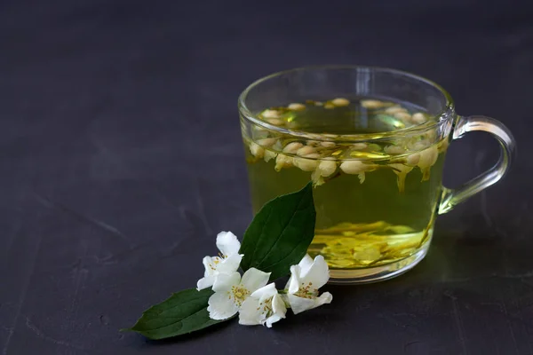 Jasmine tea. Cup of hot herbal tea with jasmine fresh flowers on a black table. Healthy lifestyle. glass cup of green tea with leaves on a black background. Hot drinks. copy space