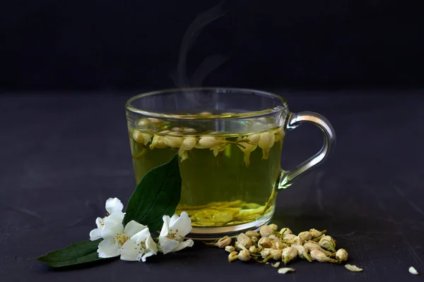 Jasmine tea. Cup of hot herbal tea with jasmine fresh flowers on a black table. Healthy lifestyle. glass cup of green tea with dry leaves on a black background. Hot drinks