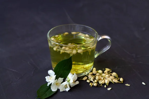 Jasmine tea. Cup of hot herbal tea with jasmine fresh flowers on a black table. Healthy lifestyle. glass cup of green tea with dry leaves on a black background. Hot drinks.