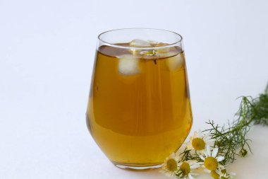 Papatya çayı. Fotokopi alanı olan beyaz bir masada buzlu bitkisel papatya çayı. Taze çiçekli bir fincan çay ve beyaz arka planda yeşil yapraklar..