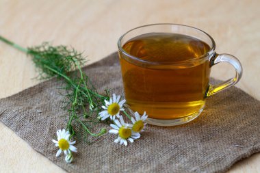 Bir kupa papatya çayı ve çuval bezi. Ahşap bir masada, üzerinde taze çiçekler ve açık arkaplanda yeşil yapraklar olan bir bardak sıcak bitkisel papatya çayı. sıcak içecekler. 