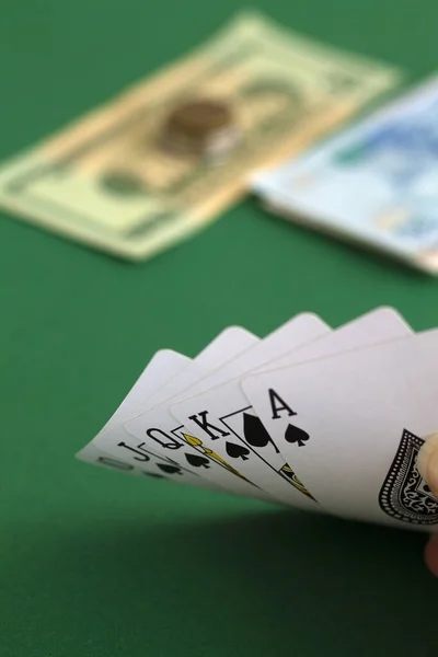 poker cards and money.hand shows a card of flush royal of black in casino. playing cards with blue deck on the green table. combination of cards on a green casino desk background.copy space. vertical