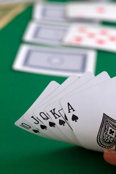 hand shows a card of royal flush of black in casino. playing cards with blue deck on the green table. combination of cards on a green casino desk background.copy space. vertical