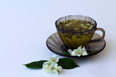 hot drinks. dark glass cup with herbal hot jasmine tea with bloom flowers of jasmine isolated on white background. healthy drink in black mug with green leaves on the table. copy space.