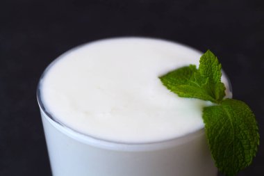 Bir bardak süt. Yakın plan Lassi içeceği ve siyah üzerine taze yeşil nane. Soğuk süt ürünleri. Hint mutfağı. kopyalama alanı. Ayran, yoğurt ve beyaz masada probiyotik. sağlıklı, mayalanmış ürünler konsepti.
