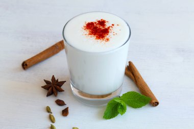 Kırmızı biberli Lassi içkisi ve beyaz arka planda taze yeşil nane. Kefir, yoğurt ya da masada probiyotik içeren süt. Baharatlı soğuk süt ürünleri: tarçın ve yıldız anason. Hint mutfağı. Boşluğu kopyala.