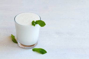 Kefir, yoğurt ya da masada probiyotik içeren süt. Beyaz arka planda taze yeşil naneli bir bardak soğuk süt Lassi içeceği. Kopya alanı olan Hint mutfağı. sağlıklı, mayalanmış ürünler konsepti.