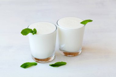 Beyaz arka planda taze yeşil naneli iki bardak soğuk süt Lassi içeceği. sağlıklı, mayalanmış ürünler konsepti. Kefir, yoğurt ya da masada probiyotik içeren süt. Hint mutfağı. Boşluğu kopyala