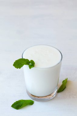 Beyaz arka planda taze yeşil naneli bir bardak soğuk süt Lassi içeceği. sağlıklı, mayalanmış ürünler konsepti. Uzayı kopyala Kefir, yoğurt ya da masada probiyotik içeren süt. Hint mutfağı. dikey
