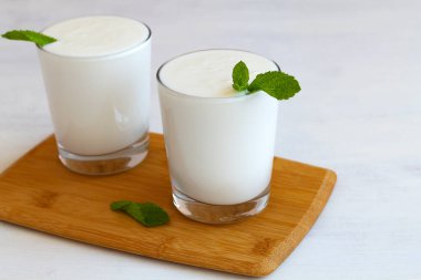 Tahta masada yeşil naneli iki bardak yoğurt. Taze süt içeceği. Sağlıklı, mayalanmış ürünler konsepti. Uzayı kopyala. Kefir, süt ya da Lassi masada probiyotiklerle birlikte içecek. Hint mutfağı.