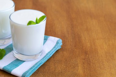 Ahşap arka planda yeşil naneli beyaz Lassi içeceği. Probiyotik soğuk süt içeceği. sağlıklı, mayalanmış ürünler konsepti. Uzayı kopyala Kefir, süt ya da yoğurt, masada probiyotikler. Hint mutfağı
