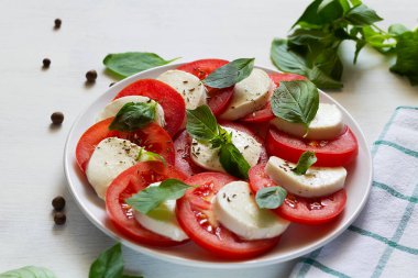 Domatesli salata ve mozzarella. İtalyan caprese salatası. Dilimlenmiş domates, mozarella peyniri, yeşil fesleğen, beyaz arka planda zeytinyağı. Kopya alanı olan taze salata.