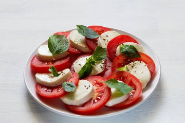 Domatesli salata ve mozzarella. Yakın plan İtalyan Caprese salatası. Dilimlenmiş domates, mozarella peyniri, yeşil fesleğen, beyaz arka planda zeytinyağı. Kopya alanı olan taze salata.