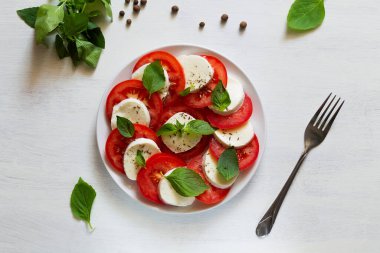 Domates ve fesleğenli salata. Baharatlı geleneksel İtalyan Caprese salatası. Dilimlenmiş domates, mozzarella, yeşil fesleğen, beyaz arka planda zeytinyağı. Fotokopi alanı olan taze salata. Üst görünüm.