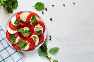 Fesleğen yapraklı domates salatası dilimlenmiş domates, mozzarella, yeşil fesleğen, beyaz arka planda zeytinyağı. Geleneksel İtalyan caprese salatalı beyaz tabak. Fotokopi alanı olan taze salata. Üst görünüm.