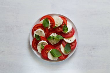Geleneksel İtalyan caprese salatası dilimlenmiş domates, mozzarella, fesleğen, beyaz arka planda zeytinyağı. Fotokopi alanı olan beyaz tabakta taze salata. Üst görünüm.